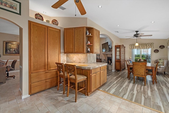 kitchen featuring ceiling fan, backsplash, kitchen peninsula, decorative light fixtures, and a breakfast bar area