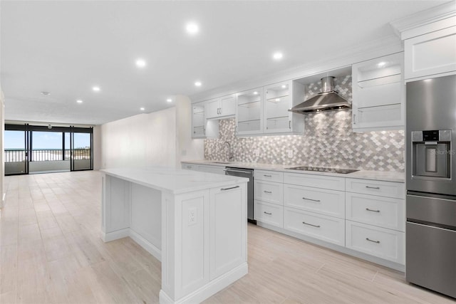 kitchen featuring white cabinets, appliances with stainless steel finishes, wall chimney exhaust hood, a kitchen island, and decorative backsplash