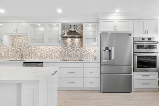 kitchen featuring appliances with stainless steel finishes, white cabinetry, tasteful backsplash, and wall chimney range hood