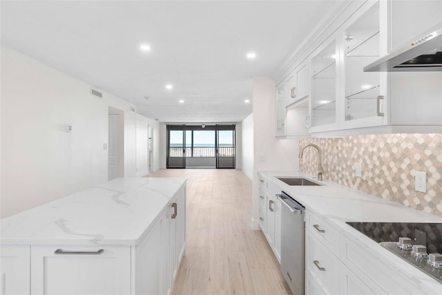 kitchen with dishwasher, wall chimney range hood, white cabinets, light stone counters, and sink