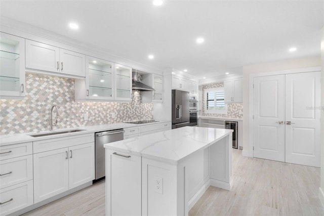 kitchen with appliances with stainless steel finishes, sink, wall chimney range hood, white cabinets, and a center island