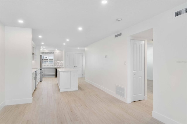 kitchen featuring light hardwood / wood-style floors, tasteful backsplash, stainless steel refrigerator, a kitchen island, and white cabinets