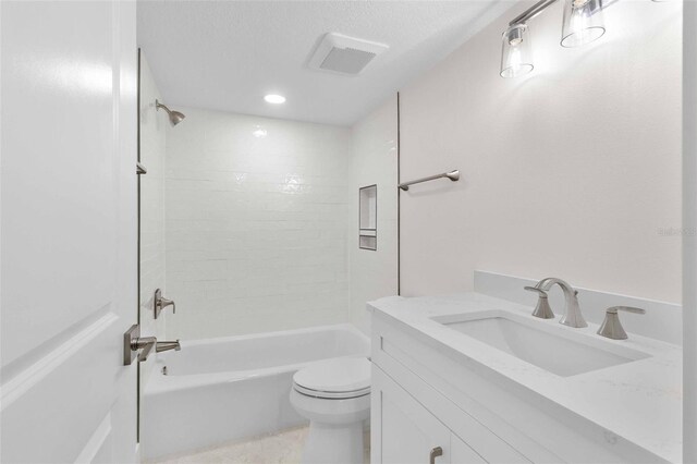 full bathroom with a textured ceiling, toilet, vanity, and tiled shower / bath