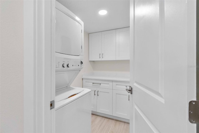 laundry area featuring cabinets, stacked washer / dryer, and light hardwood / wood-style flooring