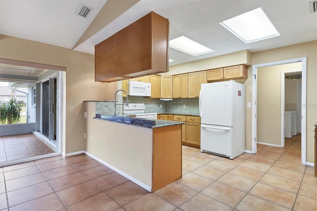 kitchen with a skylight, dark stone counters, white appliances, decorative backsplash, and light tile patterned floors