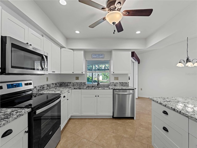 kitchen with light tile patterned floors, appliances with stainless steel finishes, white cabinets, a sink, and light stone countertops