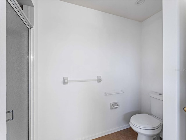 bathroom featuring tile patterned flooring, baseboards, a shower with shower door, and toilet