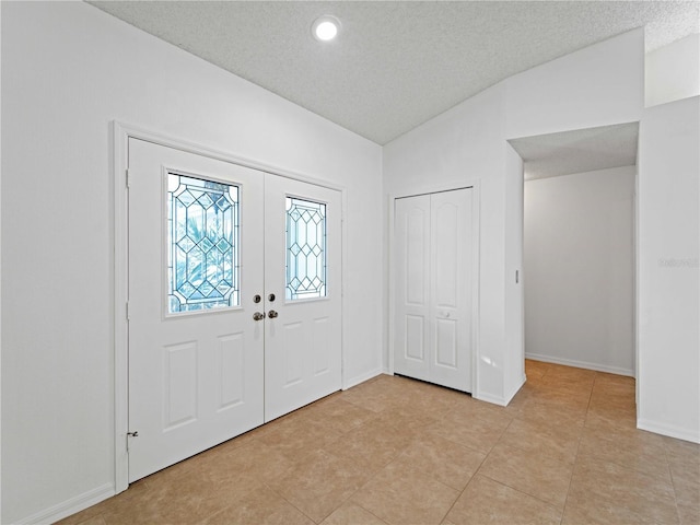 entrance foyer featuring lofted ceiling, french doors, a textured ceiling, and baseboards