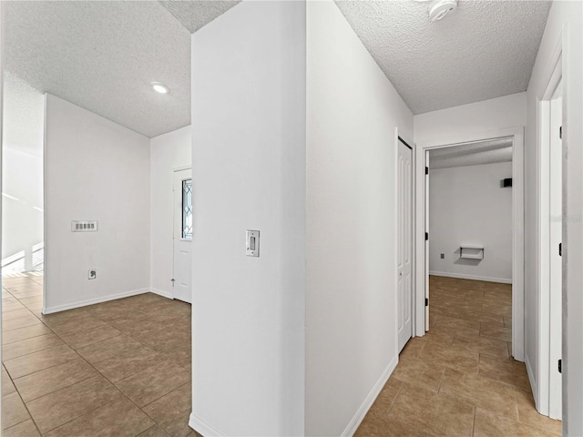 hall featuring tile patterned flooring, a textured ceiling, and baseboards