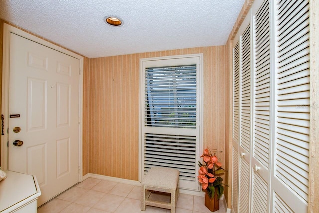 entryway with light tile patterned floors, a textured ceiling, and wood walls