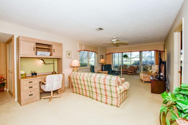 carpeted living room with ceiling fan, built in desk, and a textured ceiling