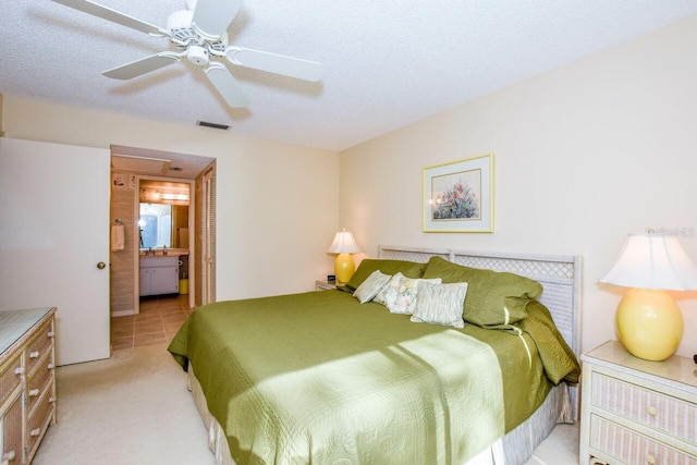 bedroom featuring ceiling fan, light colored carpet, a textured ceiling, and ensuite bath