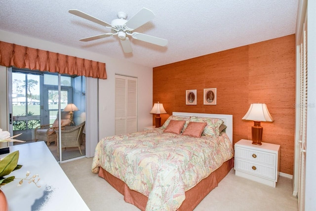 bedroom with a textured ceiling, light colored carpet, ceiling fan, wooden walls, and a closet