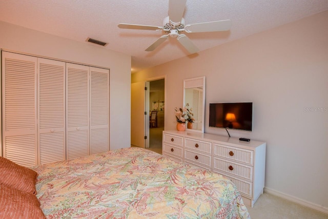 bedroom with ceiling fan, a closet, light colored carpet, and a textured ceiling