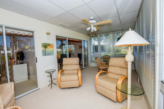 living area featuring carpet floors, a drop ceiling, and ceiling fan