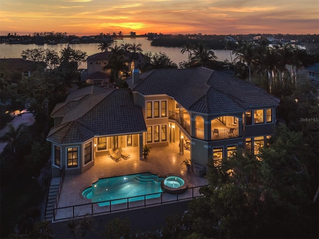 back house at dusk featuring central AC, a balcony, a patio area, a swimming pool with hot tub, and a water view