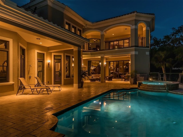 pool at night featuring an in ground hot tub and a patio