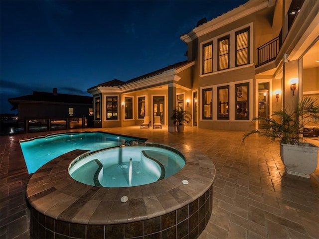 pool at twilight with an in ground hot tub and a patio