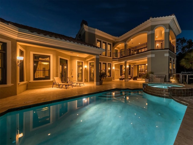 pool at night with a patio area and an in ground hot tub