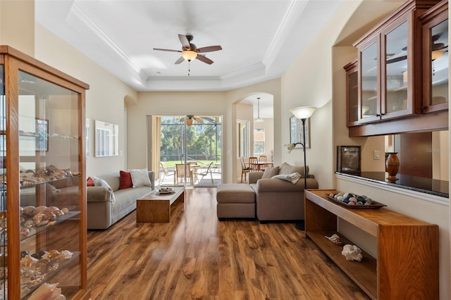 living room with dark hardwood / wood-style floors, ceiling fan, ornamental molding, and a tray ceiling