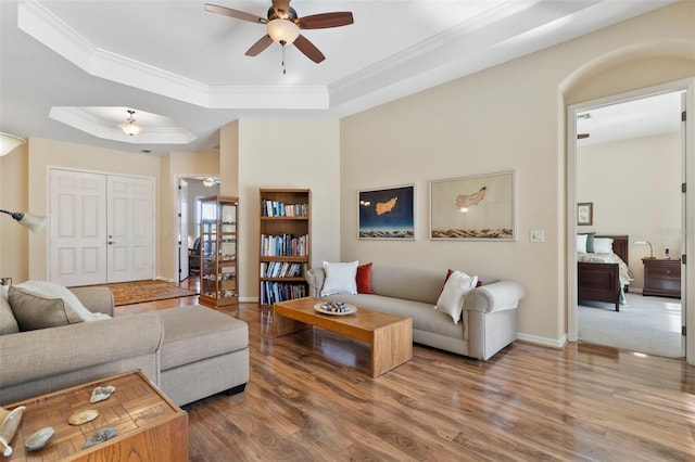 living room featuring ceiling fan, wood-type flooring, crown molding, and a tray ceiling