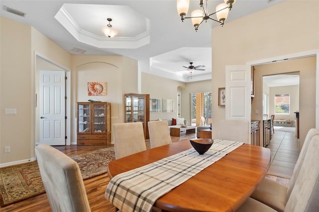 dining room featuring a raised ceiling, crown molding, wood-type flooring, and ceiling fan with notable chandelier