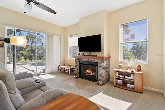 living room with ceiling fan, a stone fireplace, and light colored carpet