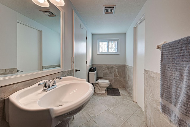 bathroom featuring sink, tile patterned floors, a textured ceiling, toilet, and tile walls