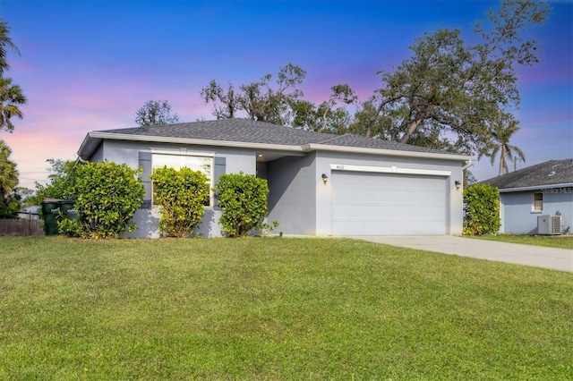 ranch-style home with central AC unit, a yard, and a garage