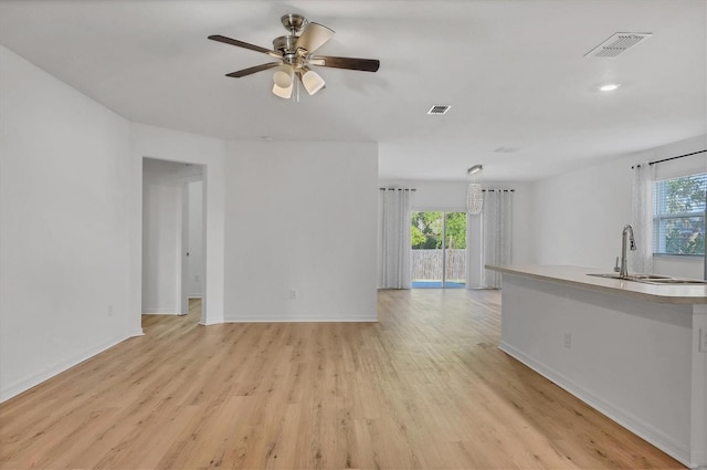 unfurnished living room with sink, ceiling fan, and light wood-type flooring