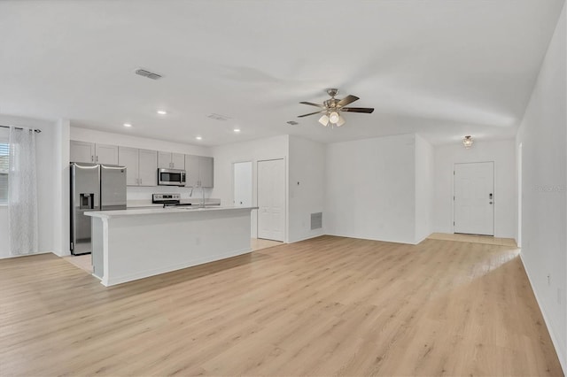 kitchen featuring gray cabinets, a center island with sink, stainless steel appliances, light wood-type flooring, and ceiling fan