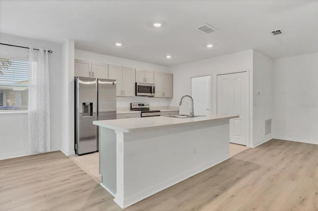 kitchen featuring an island with sink, appliances with stainless steel finishes, light hardwood / wood-style flooring, and sink