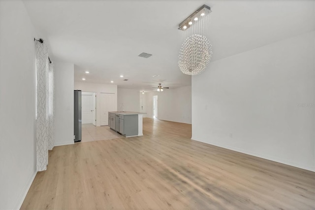 unfurnished living room with sink, light wood-type flooring, and ceiling fan with notable chandelier