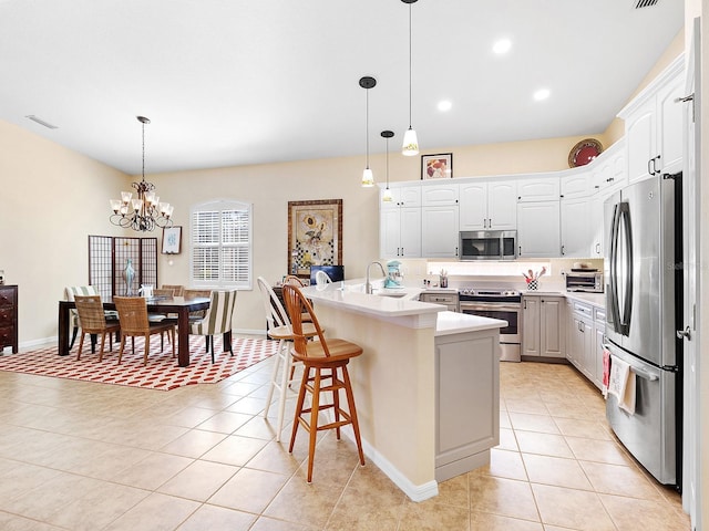 kitchen with hanging light fixtures, white cabinetry, stainless steel appliances, and a kitchen island with sink