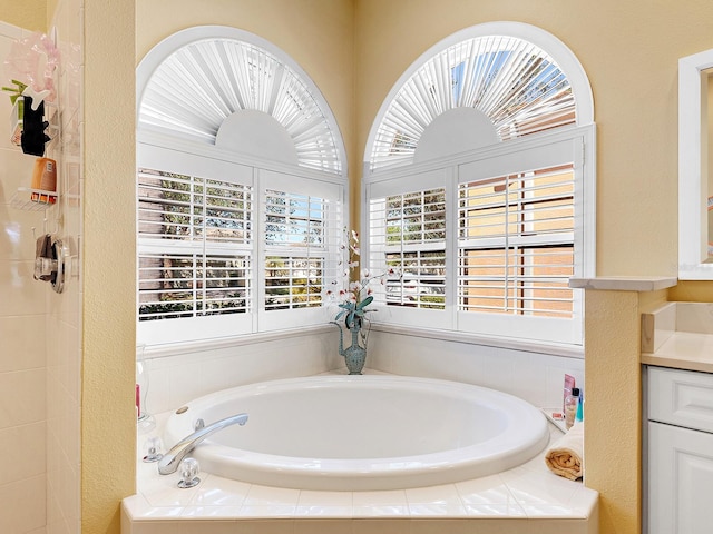 bathroom featuring tiled bath, a wealth of natural light, and vanity