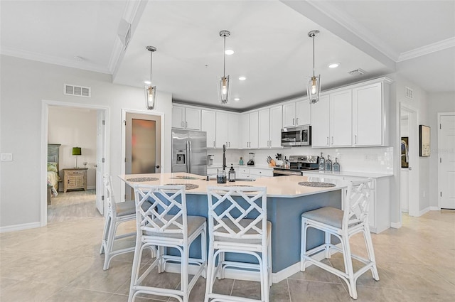 kitchen featuring appliances with stainless steel finishes, white cabinetry, pendant lighting, and an island with sink