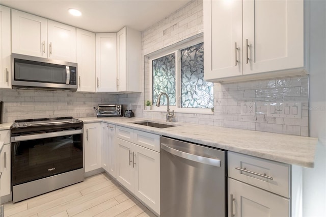 kitchen with light stone countertops, stainless steel appliances, white cabinetry, and sink