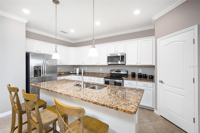 kitchen with appliances with stainless steel finishes, sink, white cabinets, hanging light fixtures, and an island with sink