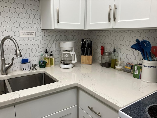 kitchen with white cabinets, tasteful backsplash, light stone countertops, and sink