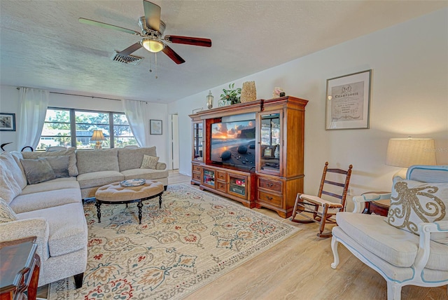 living room with ceiling fan, light hardwood / wood-style floors, and a textured ceiling