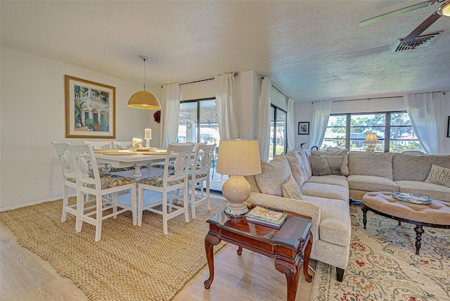 living room featuring ceiling fan, light hardwood / wood-style flooring, and a textured ceiling