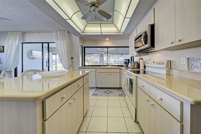 kitchen with a center island, a textured ceiling, white appliances, a tray ceiling, and light tile patterned floors