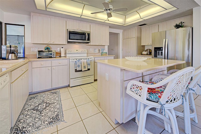 kitchen featuring stainless steel appliances, a raised ceiling, ceiling fan, light tile patterned floors, and a kitchen island