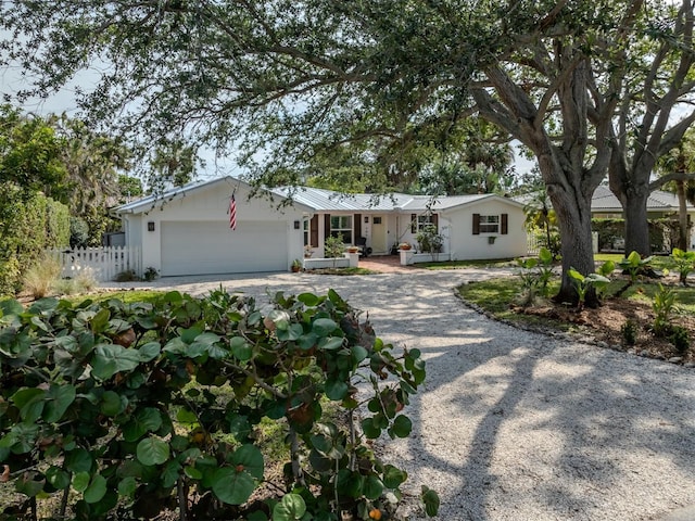 ranch-style house featuring gravel driveway, an attached garage, stucco siding, and fence