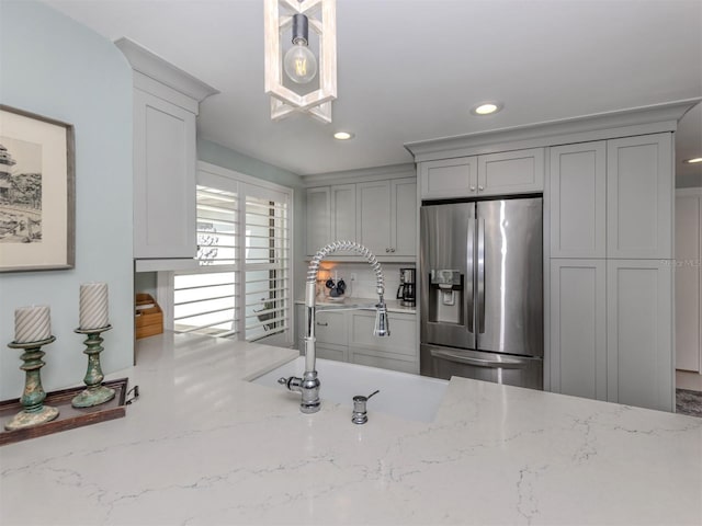 kitchen with stainless steel refrigerator with ice dispenser, gray cabinets, a sink, recessed lighting, and light stone counters
