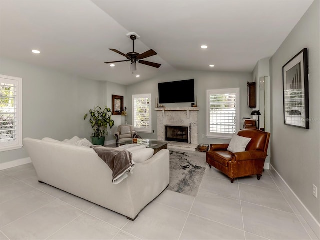 living room featuring ceiling fan, vaulted ceiling, a fireplace with raised hearth, baseboards, and light tile patterned floors