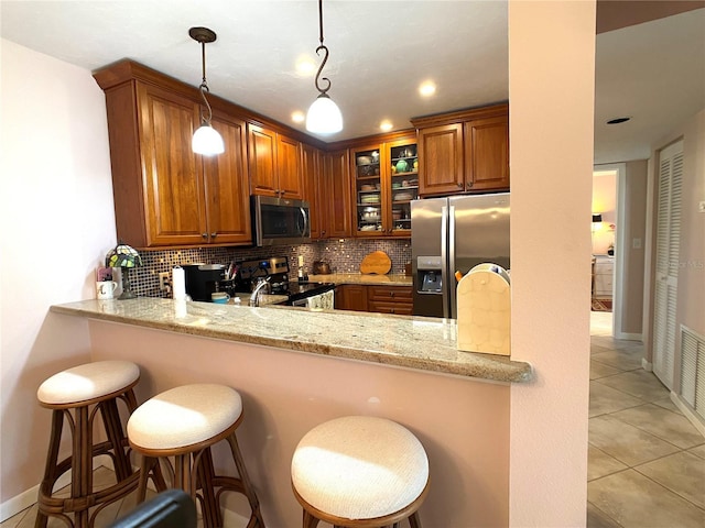 kitchen featuring kitchen peninsula, appliances with stainless steel finishes, light stone countertops, a breakfast bar, and light tile patterned floors