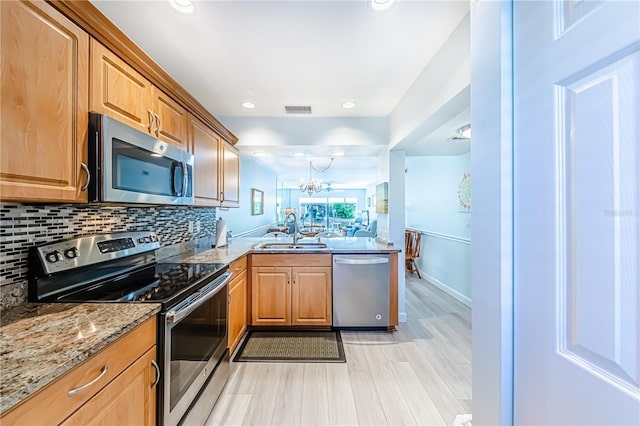 kitchen featuring sink, appliances with stainless steel finishes, a notable chandelier, light hardwood / wood-style floors, and light stone counters