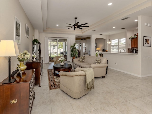 living room featuring ceiling fan, a raised ceiling, sink, and light tile patterned floors