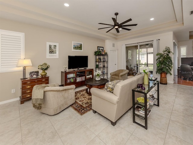 tiled living room with ceiling fan and a raised ceiling